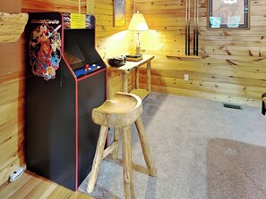 A wooden cabin interior with a Multicade arcade machine, a small table with a lamp, and a wooden stool. - A Majestic View III by Jackson Mountain Rentals (Townsend)