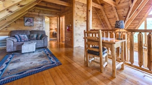 A cozy log cabin interior with a wooden ceiling, a sofa, a dining table, and a patterned rug. - A Majestic View III by Jackson Mountain Rentals (Townsend)