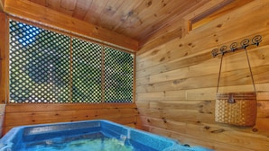 A wooden cabin with a hot tub, a window with a lattice design, and a hanging basket. - A Garden Blessing by Jackson Mountain Rentals (Gatlinburg)
