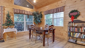 A wooden cabin interior with a dining table, chairs, a Christmas tree, and a bookshelf. - A Garden Blessing by Jackson Mountain Rentals (Gatlinburg)