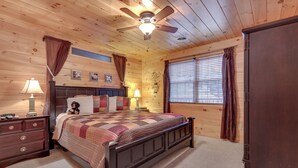 A wooden-paneled bedroom with a bed, two nightstands, a ceiling fan, and a window with blinds. - A Garden Blessing by Jackson Mountain Rentals (Gatlinburg)
