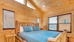 Une chambre située dans une cabane en rondins, avec un lit en bois, deux tables de chevet et de grandes fenêtres.