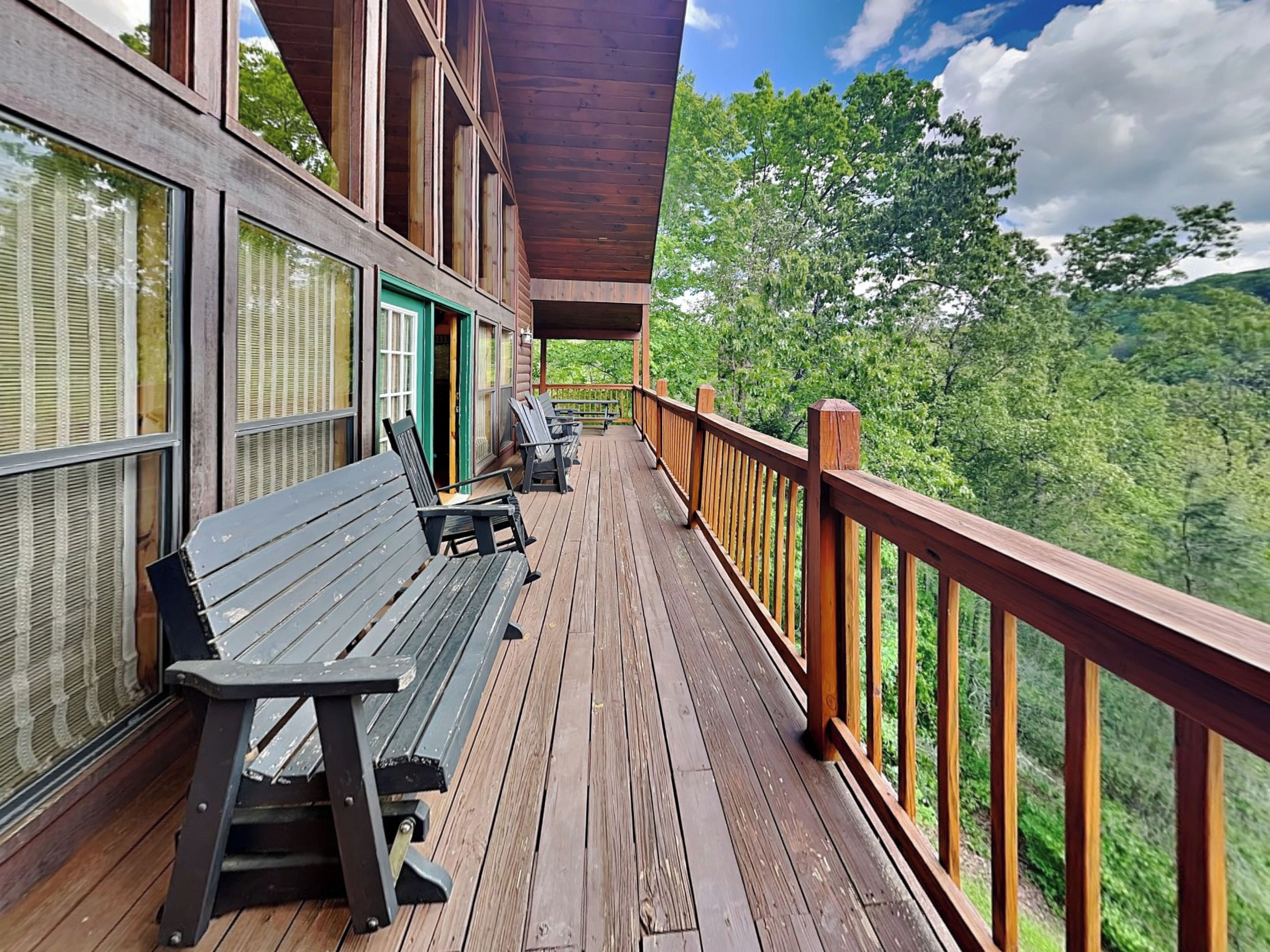 A wooden deck with benches and a railing overlooking a forested landscape.