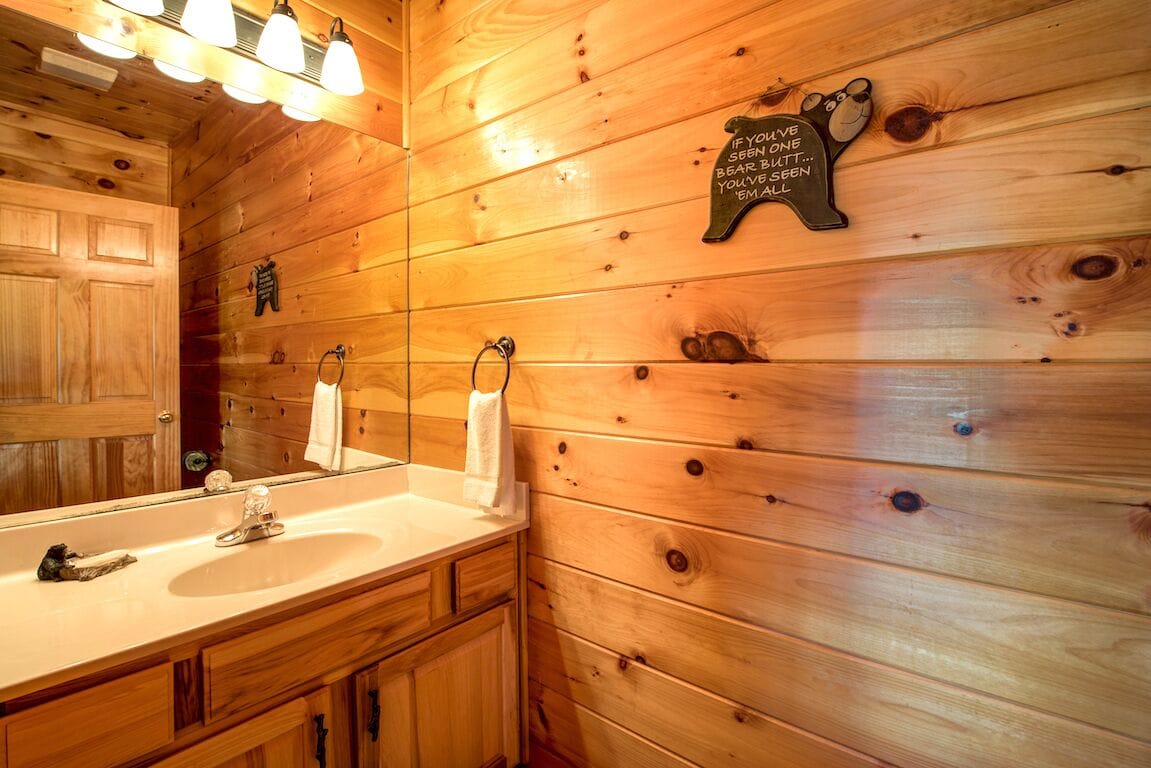 A wooden cabin-style bathroom with a large mirror, two sinks, and a towel rack.