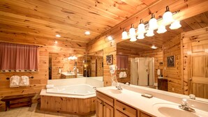 A wooden cabin-style bathroom with a large bathtub, a double sink vanity, and a mirror. - Bear Hunter by Jackson Mountain Rentals (Sevierville)