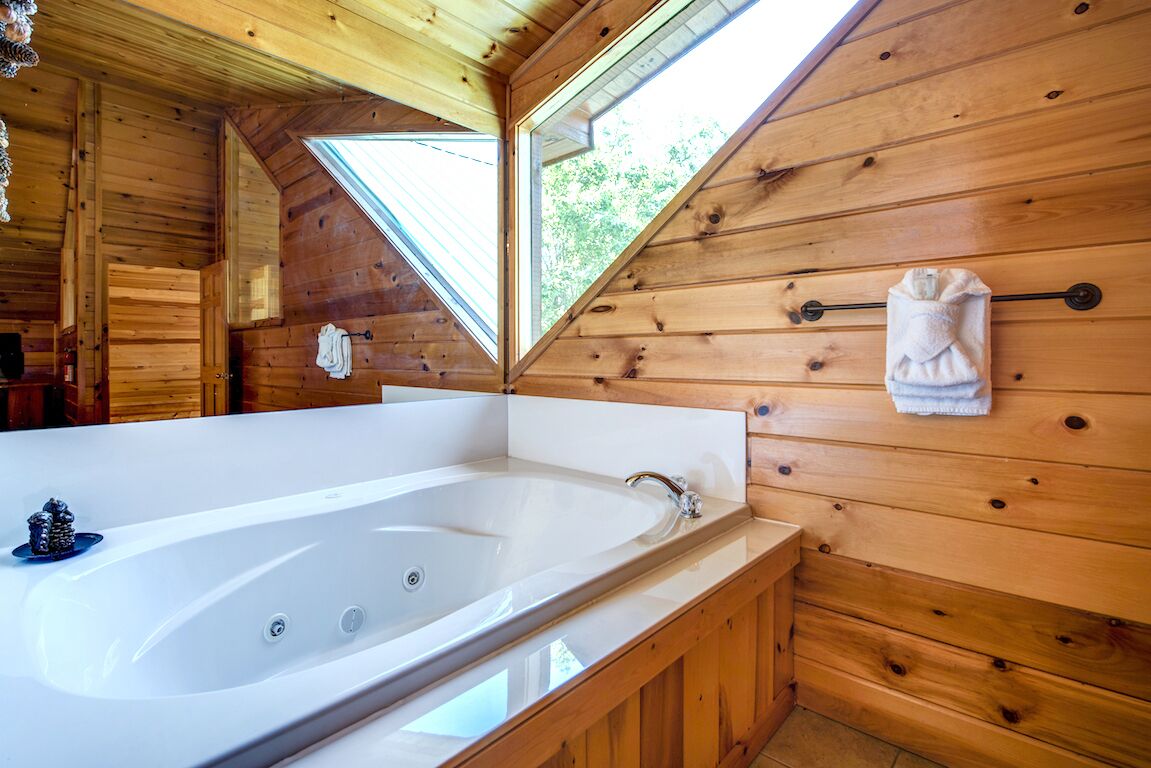 A wooden cabin with a large bathtub, wooden walls, and a skylight.