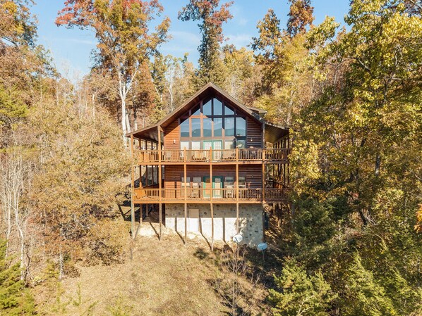 A two-story log cabin with a balcony, surrounded by trees. - Bear Hunter by Jackson Mountain Rentals (Sevierville)