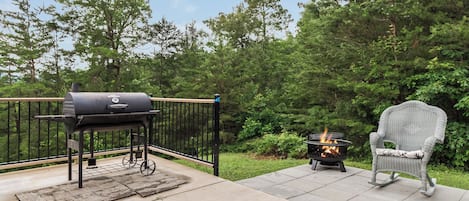 Un patio al aire libre con una parrilla, un pozo de fuego y una silla de mimbre.