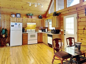 A wooden cabin-style kitchen with a refrigerator, stove, microwave, and wooden cabinets. - African Safari by Jackson Mountain Rentals (Sevierville)