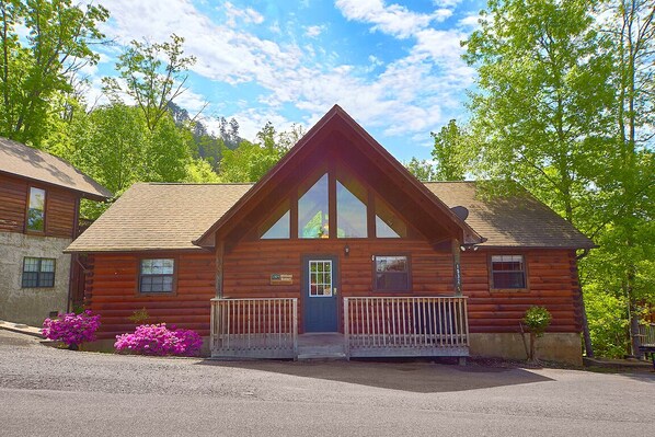A log cabin with a front porch, a small attached structure, and a mountain backdrop. - African Safari by Jackson Mountain Rentals (Sevierville)