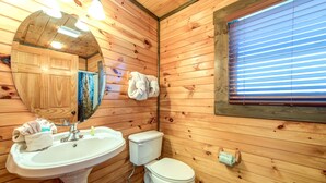 A wooden cabin bathroom with a sink, toilet, and a mirror. - Celebration Lodge by Jackson Mountain Rentals (Gatlinburg)