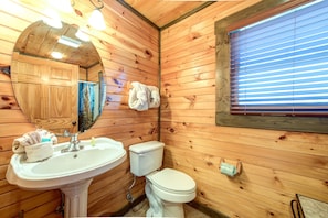 A wooden cabin bathroom with a sink, toilet, and a mirror. - Celebration Lodge by Jackson Mountain Rentals (Gatlinburg)