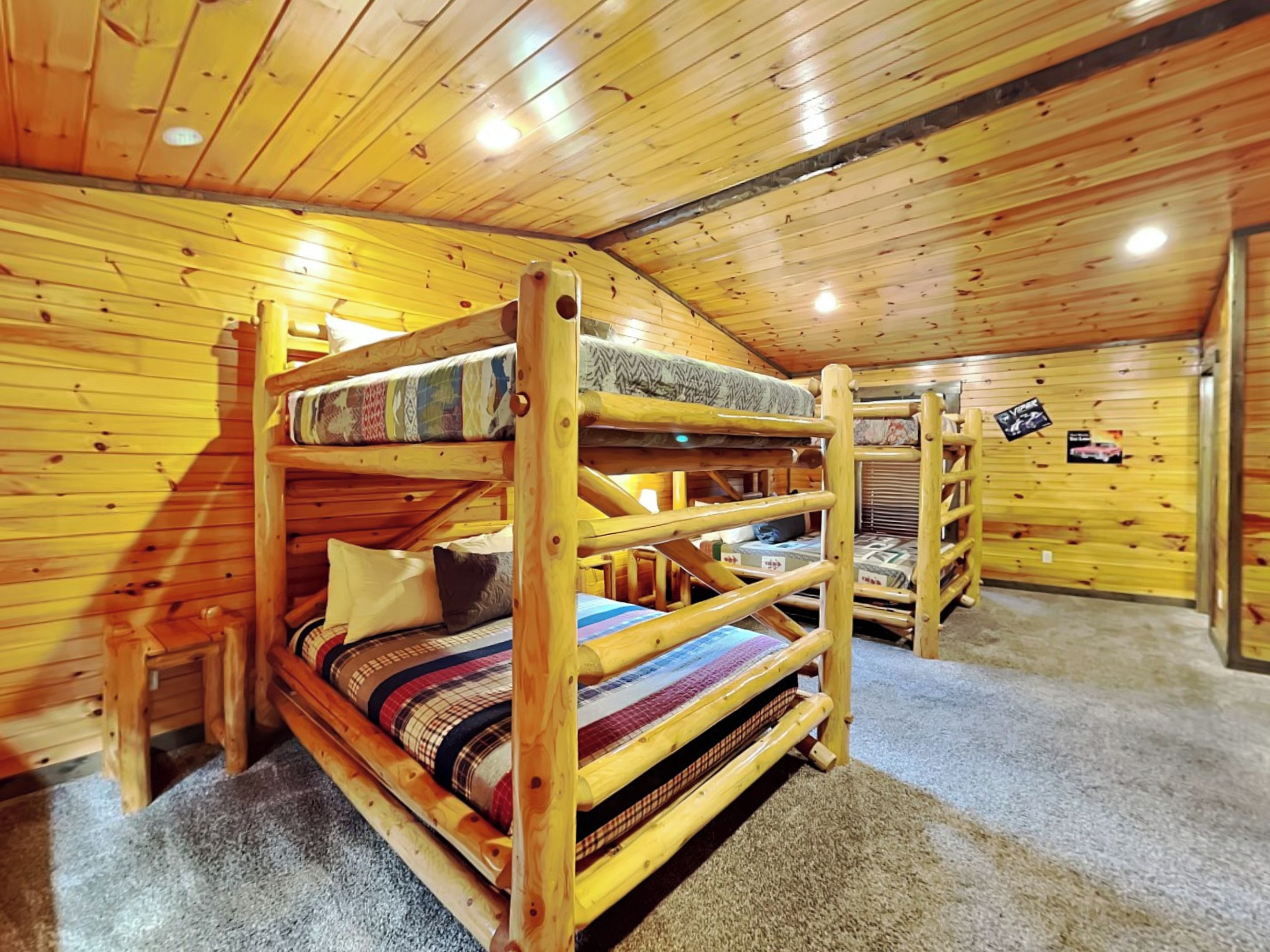 A bunk bed room with wooden walls and ceiling, carpeted floor, and a small wooden bench.
