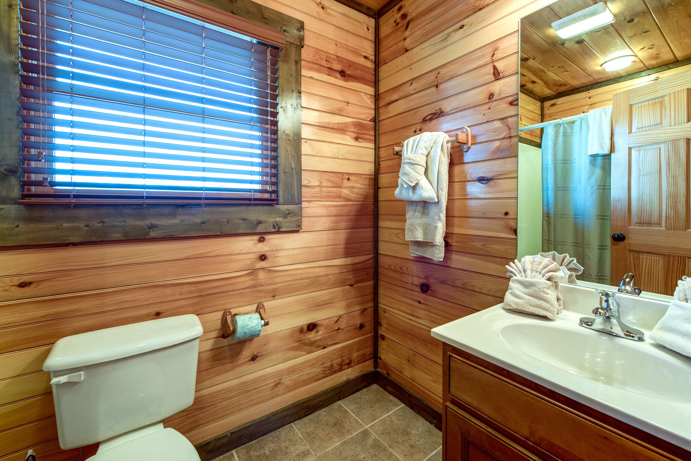 Un baño con paneles de madera, un inodoro, un lavamanos y una ventana con persianas.