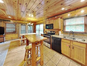 A wooden cabin interior with a kitchen area featuring wooden cabinets, a stove, a microwave, and a sink. - Celebration Lodge by Jackson Mountain Rentals (Gatlinburg)