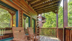 A wooden deck with rocking chairs and a covered area with a view of a cabin. - Celebration Lodge by Jackson Mountain Rentals (Gatlinburg)