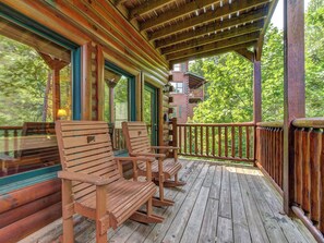 A wooden deck with rocking chairs and a covered area with a view of a cabin. - Celebration Lodge by Jackson Mountain Rentals (Gatlinburg)