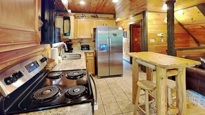 Una cocina con estufa, refrigerador, armarios de madera y una mesa de madera con taburetes.