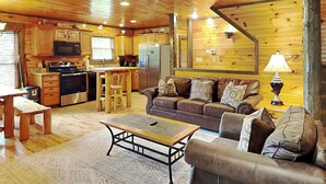 Interior acogedor de una cabaña con techo de madera, una kitchenette, un comedor y una sala de estar con sofá y mesa de centro.