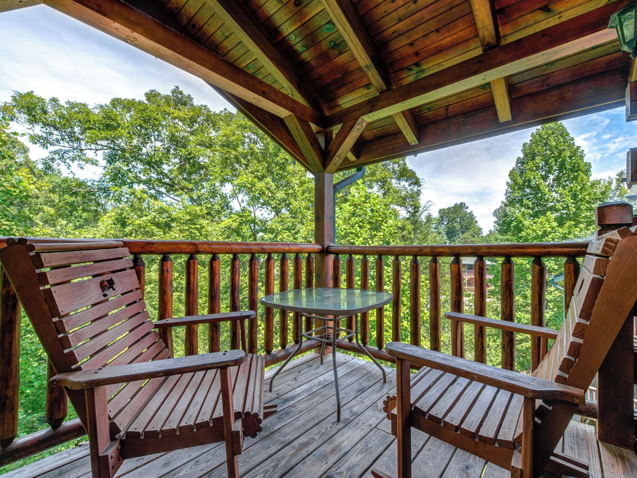 Une terrasse en bois avec une table en verre et deux chaises en bois.