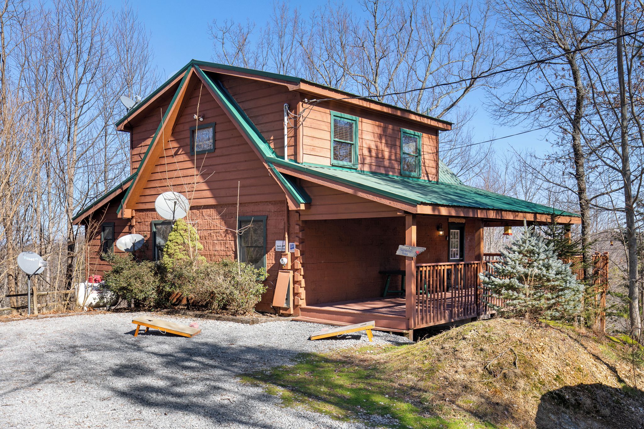 A wooden cabin with a green roof, a porch, and a satellite dish.