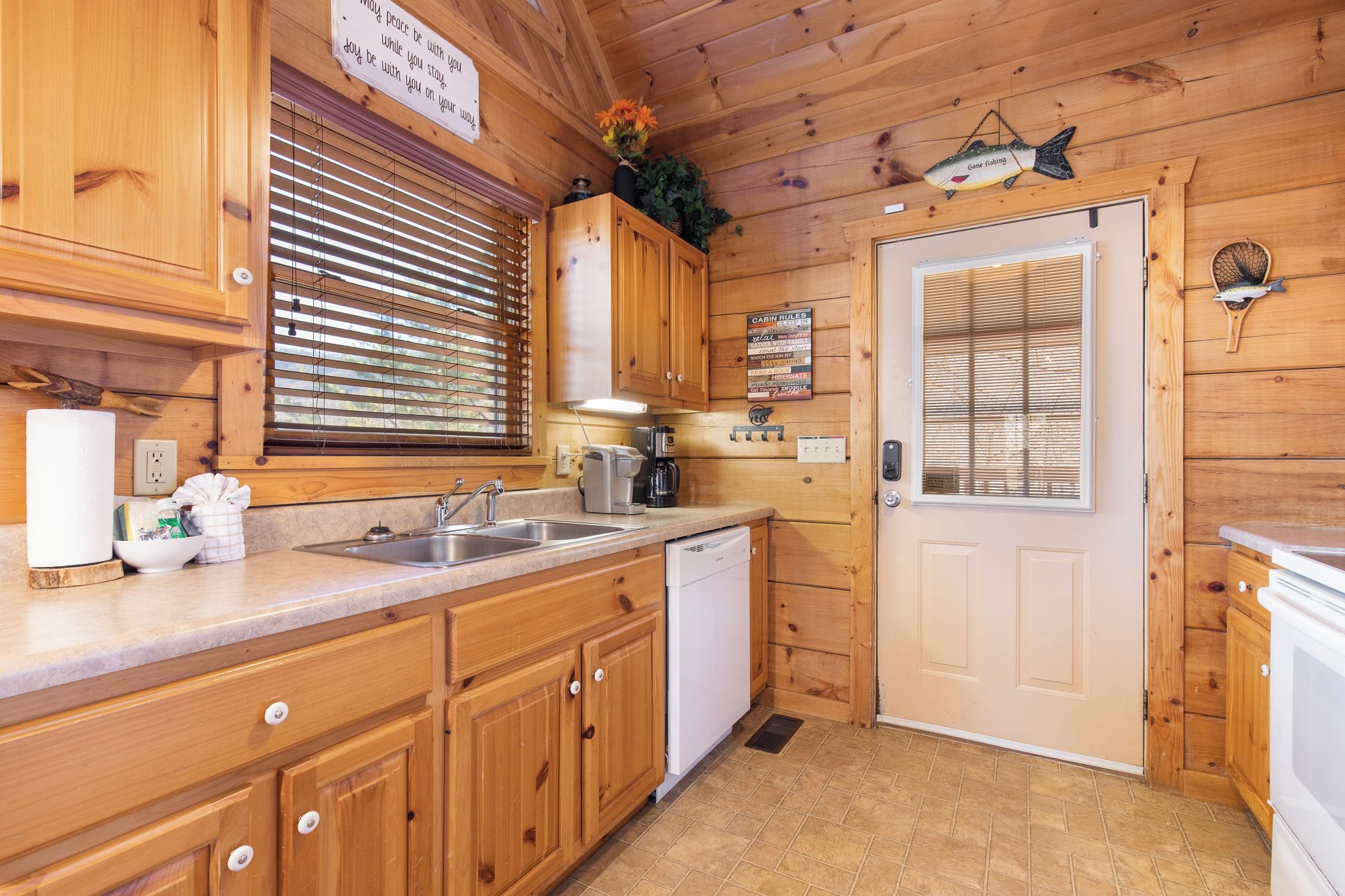 A wooden cabin-style kitchen with a sink, dishwasher, and a sign above the door.