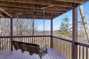 A wooden deck with a swing, surrounded by trees and a clear sky. - Huckleberry Ridge by Jackson Mountain Rentals (Pigeon Forge)