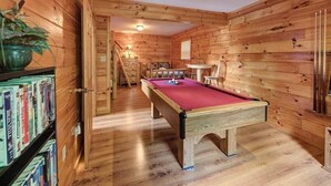 Une pièce en bois avec une table de billard, des étagères et un petit coin repas.