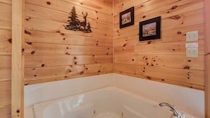 L’intérieur d’un chalet en bois, avec une grande baignoire blanche, des murs en bois et deux tableaux encadrés.