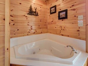 A wooden cabin interior with a large white bathtub, wooden walls, and two framed pictures. - Our Mountain Getaway by Jackson Mountain Rentals (Sevierville)
