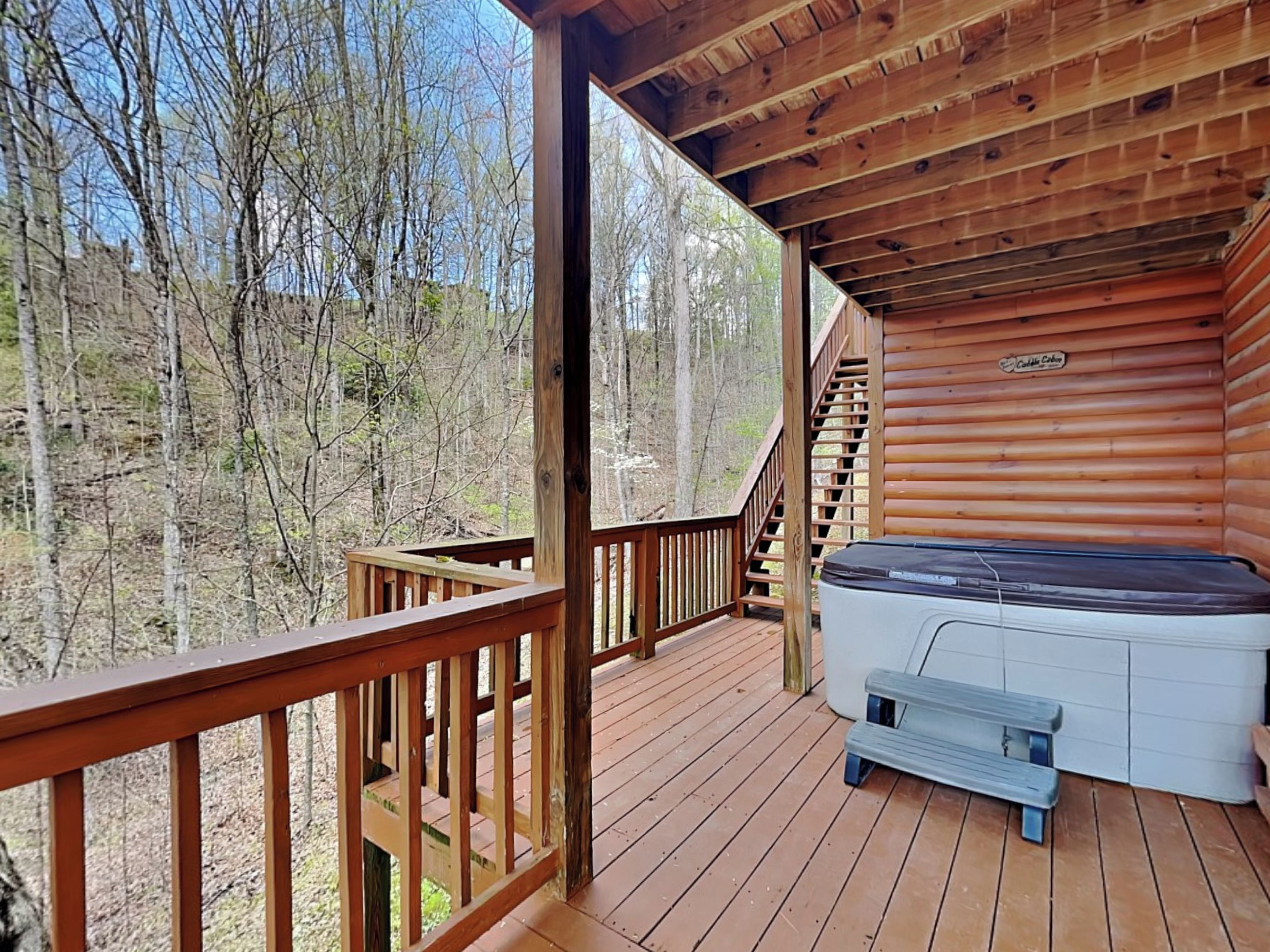A wooden deck with a hot tub, a bench, and a staircase leading to an upper level.