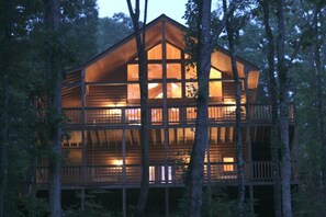 A multi-level wooden cabin with large windows and balconies, surrounded by trees.