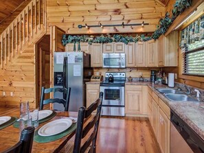 Une cuisine rustique, située dans une cabane en bois, équipée d’un réfrigérateur, d’une cuisinière, d’un four à micro-ondes et d’un évier.