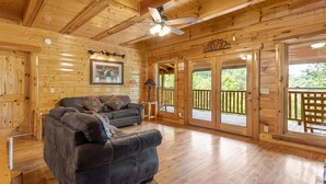 A wooden cabin interior with a leather sofa, a ceiling fan, and large glass doors leading to an outdoor deck.