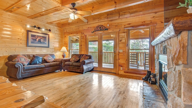 A wooden cabin interior with a large sofa, a fireplace, and a ceiling fan.