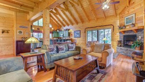 A cozy cabin interior with wooden walls, a stone fireplace, a dining area, and a living room furnished with sofas and a coffee table. - Mountain Magic by Jackson Mountain Rentals (Sevierville)