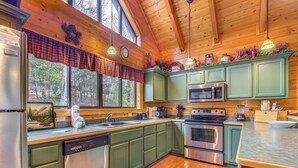 A kitchen with green cabinets, stainless steel appliances, a large window, and wooden ceiling beams. - Mountain Magic by Jackson Mountain Rentals (Sevierville)