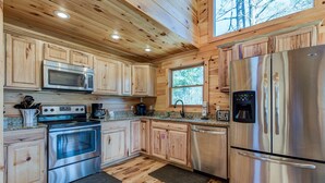 A wooden cabin kitchen with a stainless steel refrigerator, oven, microwave, and sink. - Rocky Top Lookout by Jackson Mountain Rentals (Gatlinburg)