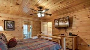 A wooden cabin bedroom with a bed, a desk, a television, and a ceiling fan. - Rocky Top Lookout by Jackson Mountain Rentals (Gatlinburg)