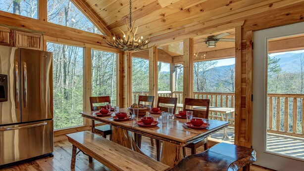 A wooden cabin with a dining area featuring a large table set for four, a refrigerator, and a bench. - Rocky Top Lookout by Jackson Mountain Rentals (Gatlinburg)
