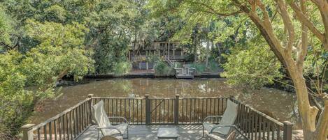 Een houten terras met vier stoelen en een tafel, met uitzicht op een rivier en een bebost gebied.