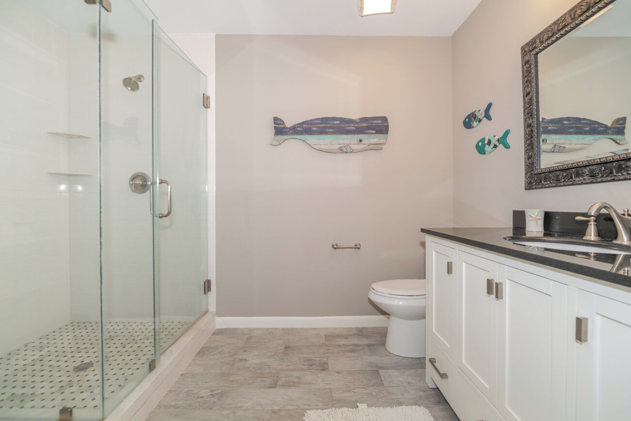 Une salle de bain avec une douche à parois de verre, des toilettes et un meuble-lavabo avec un évier et un miroir.