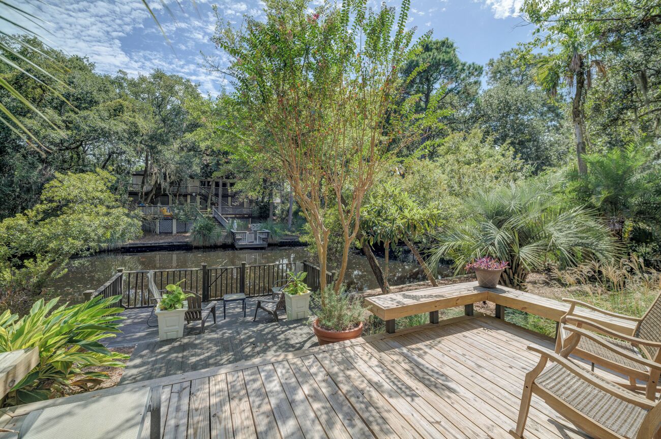 A wooden deck with outdoor furniture, a pond, and a bridge leading to a building with multiple levels.
