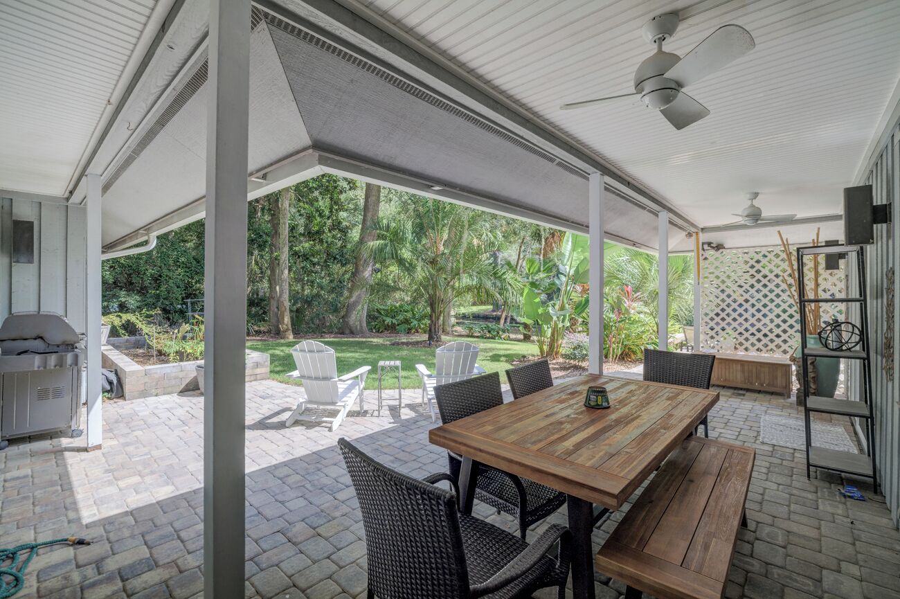 Un patio exterior con una mesa y sillas de madera, una parrilla y vistas a un jardín.