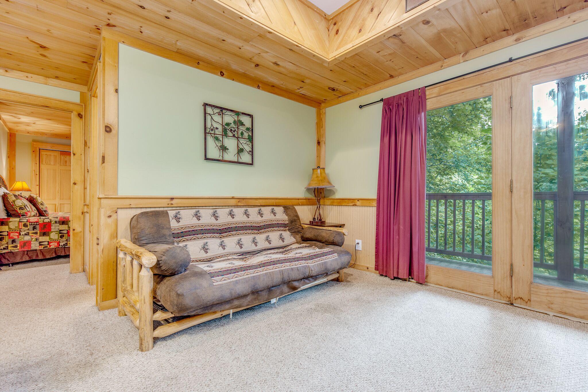 A wooden interior with a sofa, a lamp, and a large window with a view of greenery.