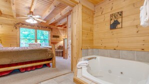 Una cabaña de madera con un dormitorio que tiene una cama, un baño con una bañera grande y un ventilador de techo.