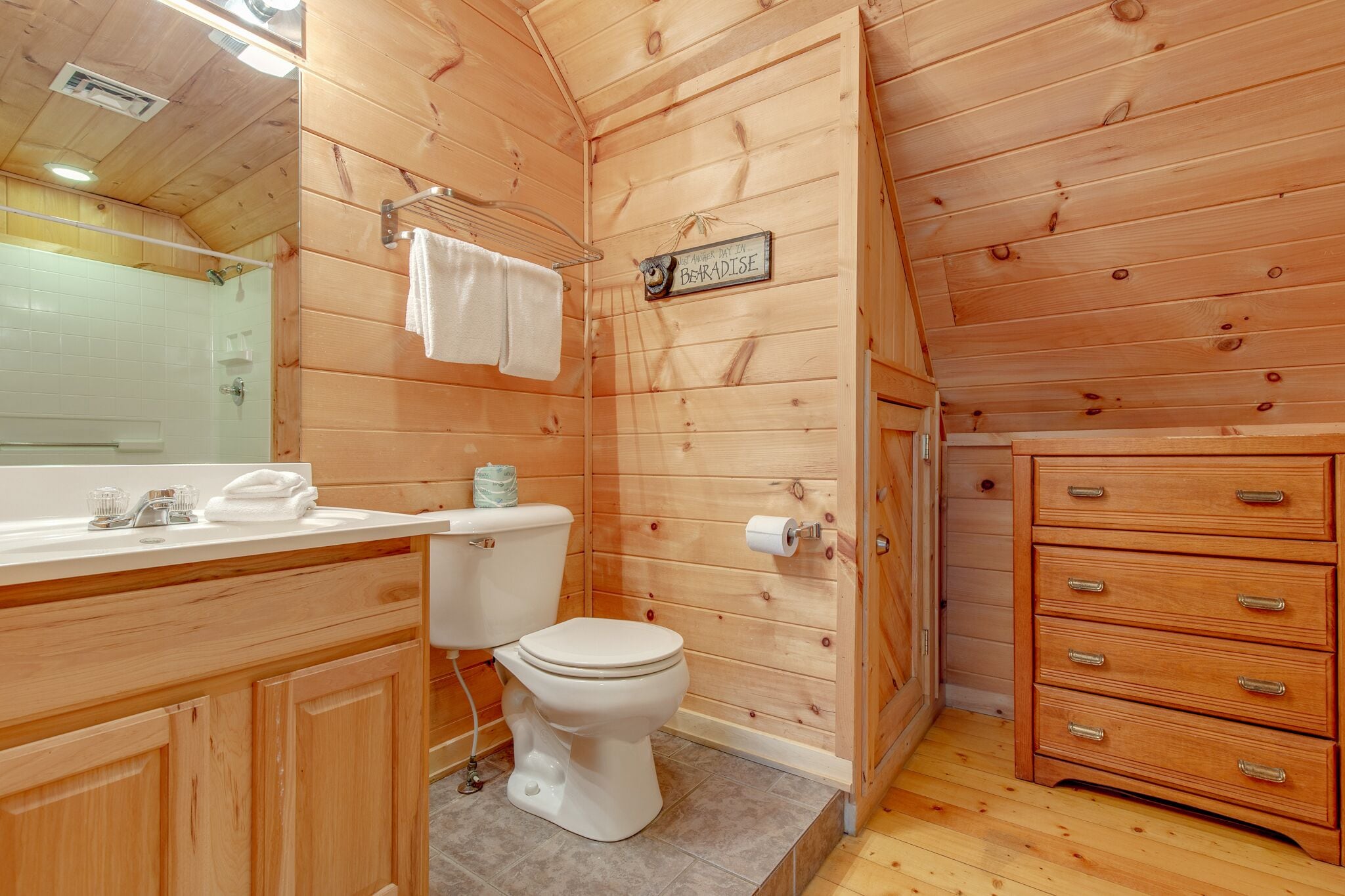 A wooden cabin bathroom with a toilet, sink, and wooden cabinets.