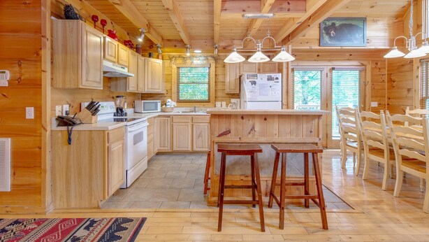 Interior de una cabaña de madera con cocina, comedor y taburetes de bar.