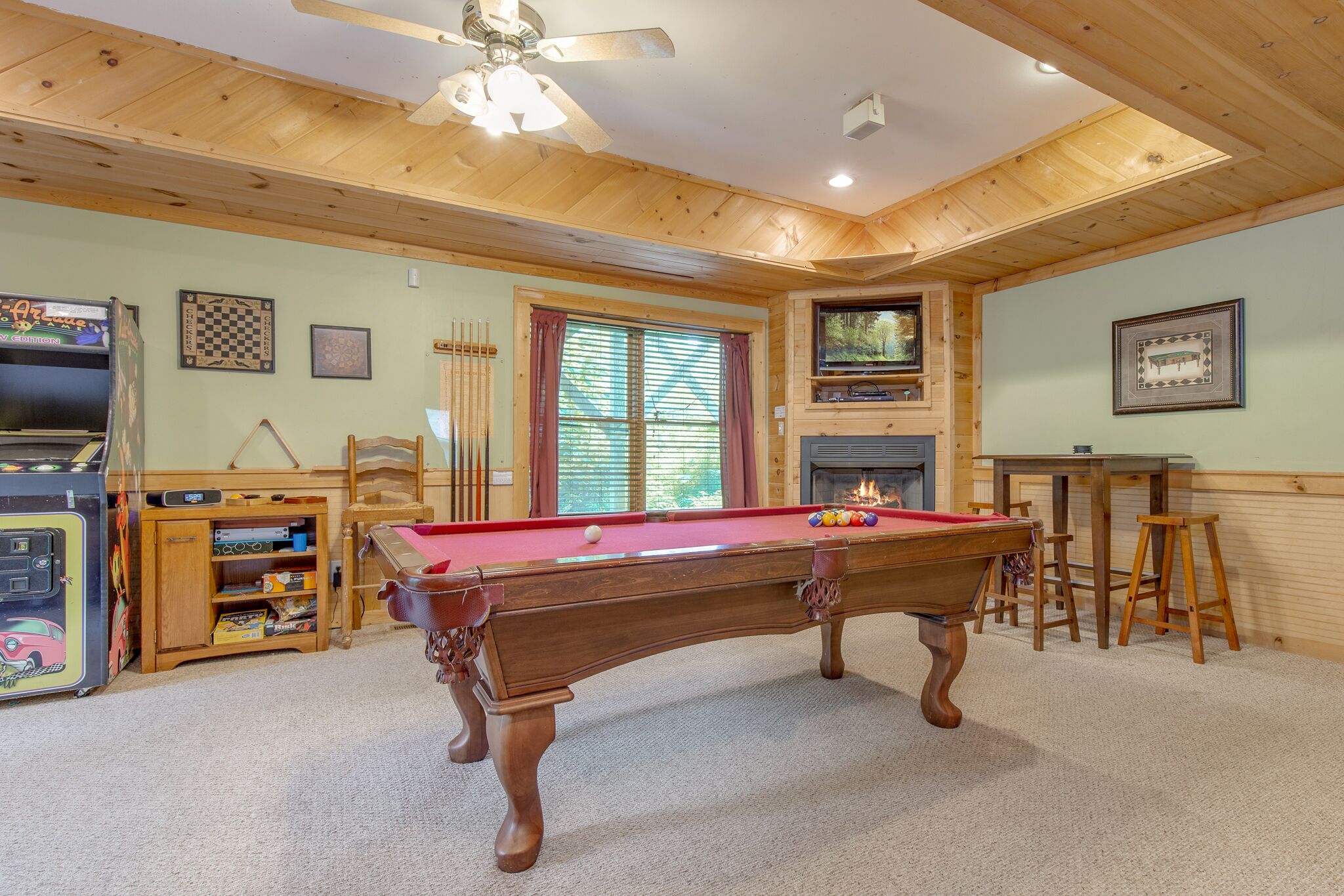 A pool table in a room with wooden ceilings and walls, a television, and a fireplace.