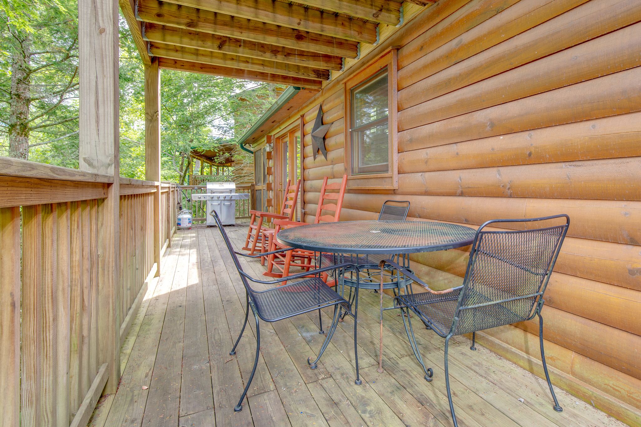 A wooden deck with a round metal table and chairs, surrounded by a wooden fence.